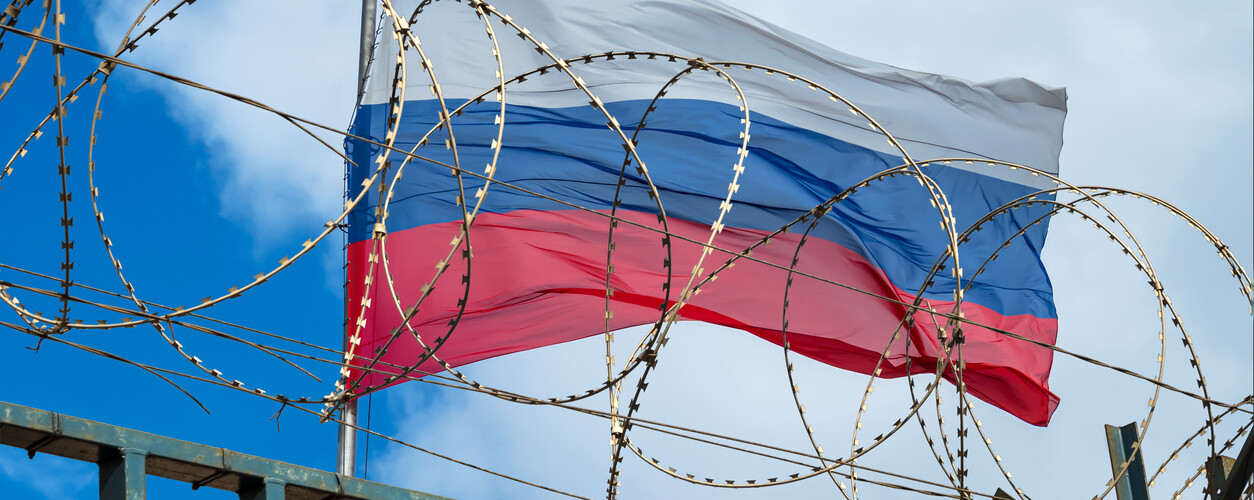 View of russian flag behind barbed wire against cloudy sky.