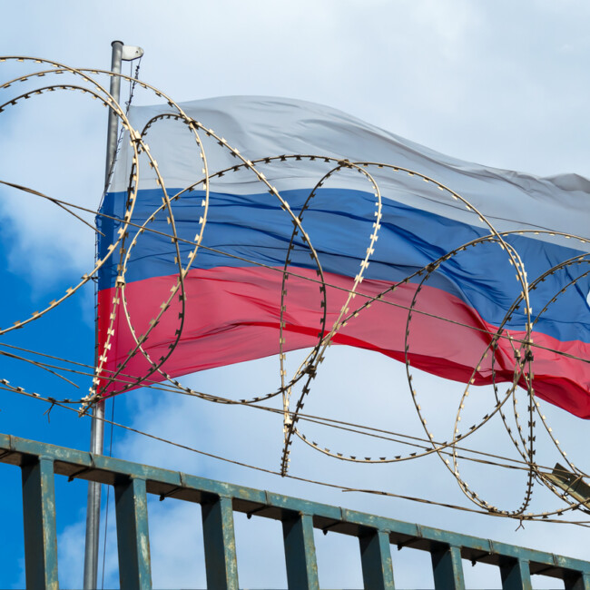 View of russian flag behind barbed wire against cloudy sky.