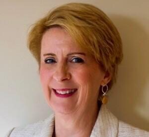 Deborah McCarthy smiling at the camera, a beige suit on.