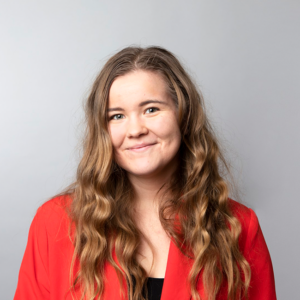 Anna Majuri, brown curly hair, red suit, smiling.