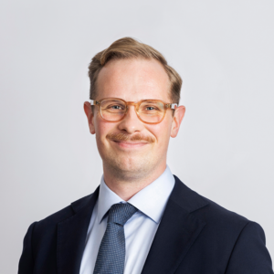 Picture of Joel Linnainmäki, smiling face, brown glasses, light brown hair, black suit.