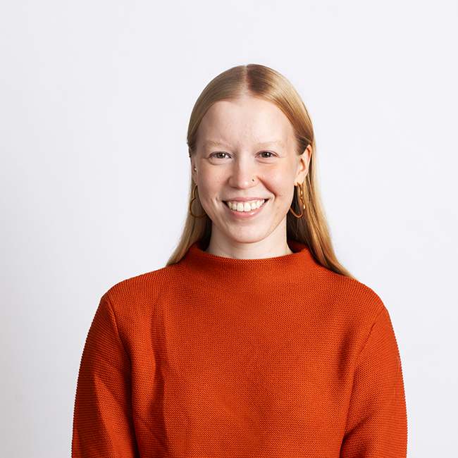 Picture of Anna Kananen, blonde hair, orange shirt, smiley face.