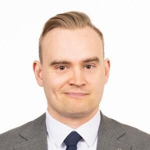 Atte Harjanne looking at the camera with a black and white wool suit on, white background.