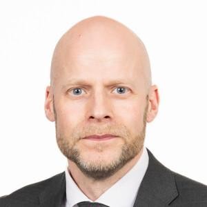 Aleksi Jäntti looking at the camera with a grey suit on, white background.