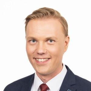 Jani Kokko looking at the camera with a blue suit on, white background.