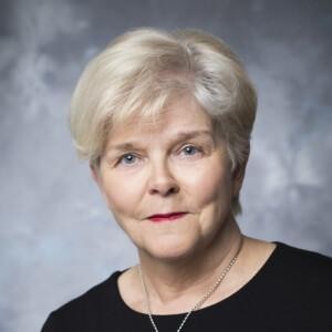 Paula Vanninen looking at the camera with a silver necklace and a black blouse on.