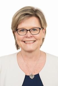 Sari Tanus looking at the camera with a black and white blouse on, white background.