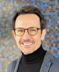 Radoslav Dimitrov smiling at the camera with glasses on his face and a gray suit jacket on.