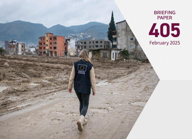 Cover photo for the publication. A person wearing an EU vest walks towards destroyed buildings in the Hatay region, one of the areas severely damaged by the February 2023 earthquakes.