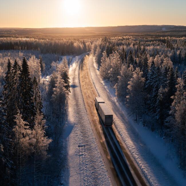 Cargo truck on a highway in winter landscape against sunset. Delivery and transportation in Northern Europe.