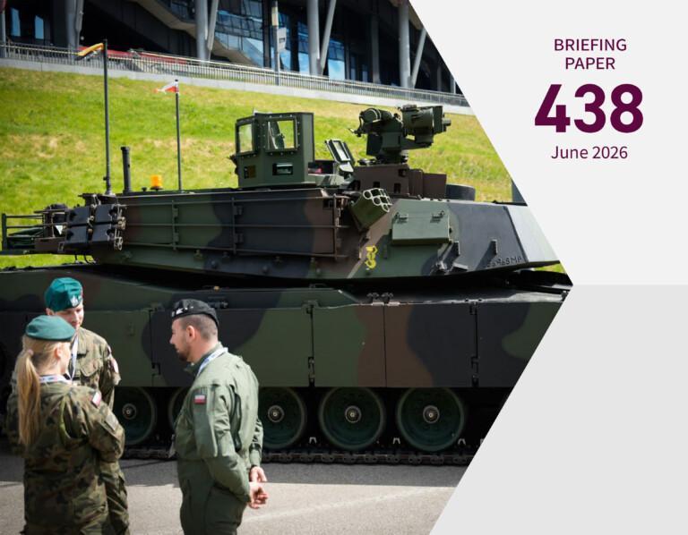 Military personnel talking to each other while standing with their backs to the camera in front of a military tank.