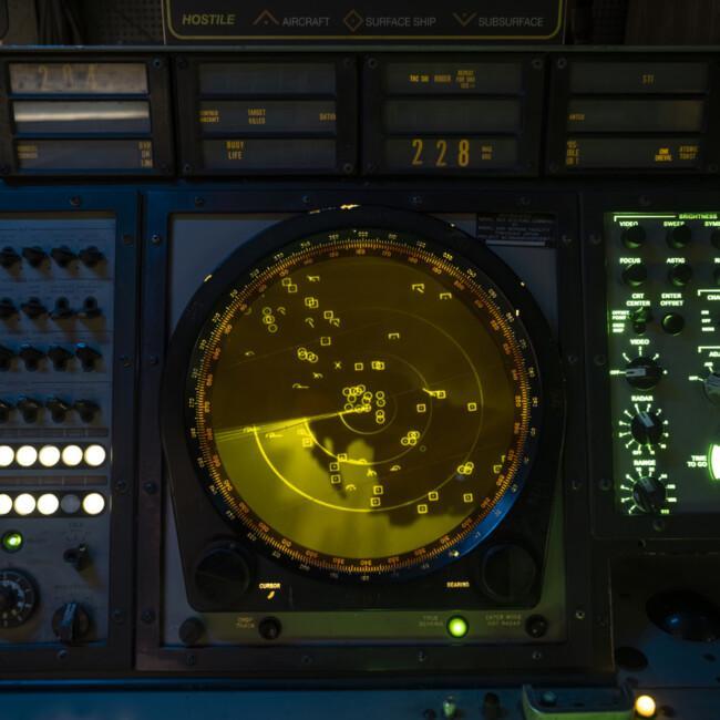 Professional military radar display screen showing yellow scope with targets and control panels in command center.