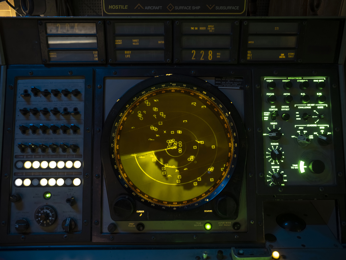 Professional military radar display screen showing yellow scope with targets and control panels in command center.