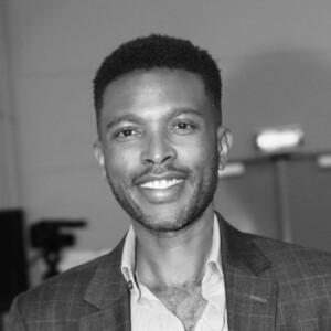 Black and white photo of Kennedy Mbeva smiling at the camera with a suit on.
