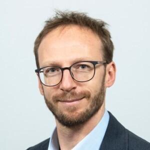 Marcin Kaczmarski smiling at the camera, wearing a suit.