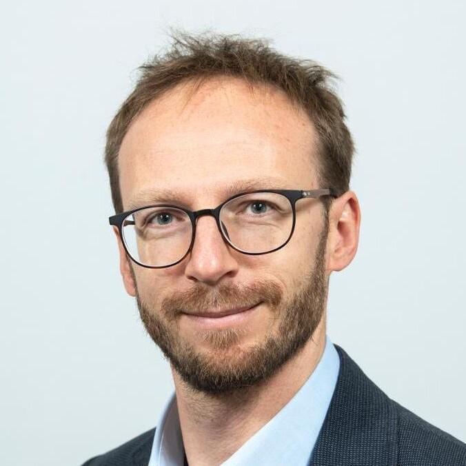 Marcin Kaczmarski smiling at the camera, wearing a suit.