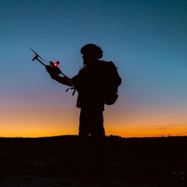 Silhouettes of soldiers are using drone for scouting during military operation against the backdrop of a sunset. Application of modern technology during war.