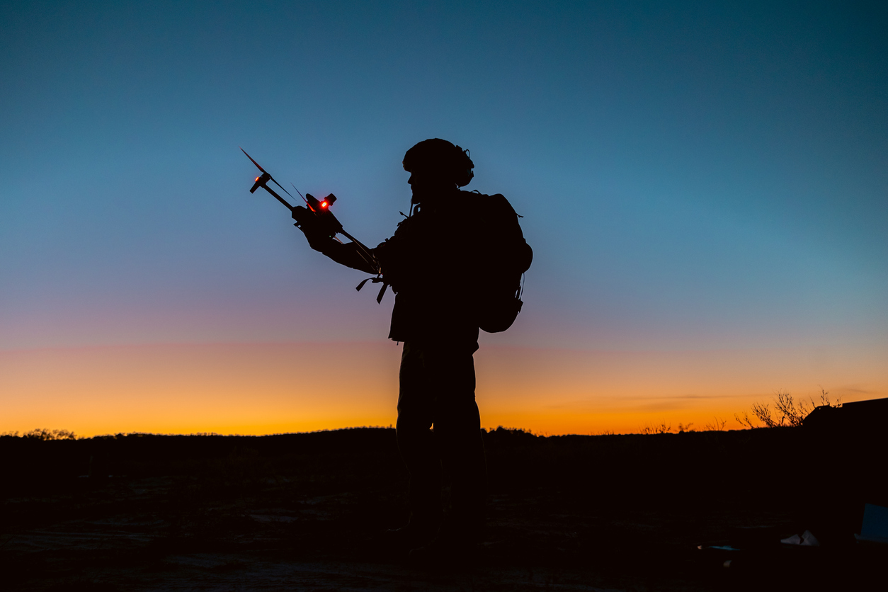 Silhouettes of soldiers are using drone for scouting during military operation against the backdrop of a sunset. Application of modern technology during war.